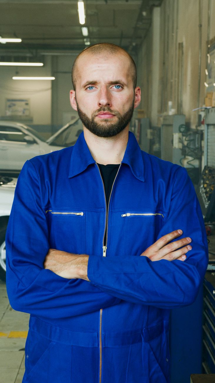 Mechanic in a blue uniform standing with arms crossed in the garage